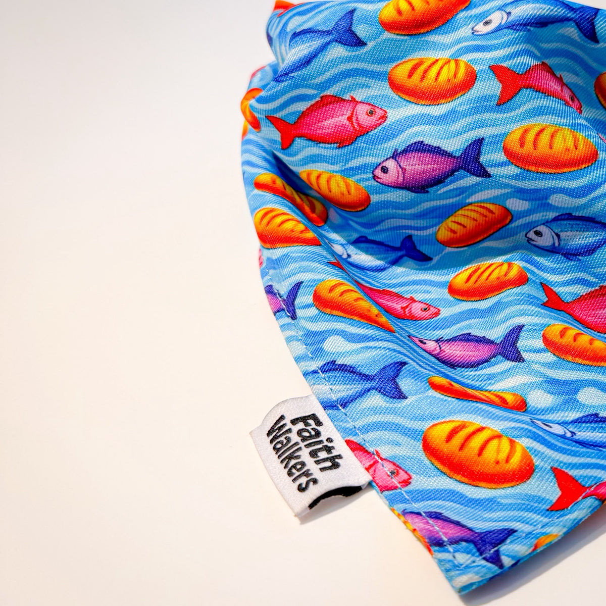 Close-up of the blue Loaves and Fishes bandana with colorful fish, bread loaves and a Faith Walkers label.